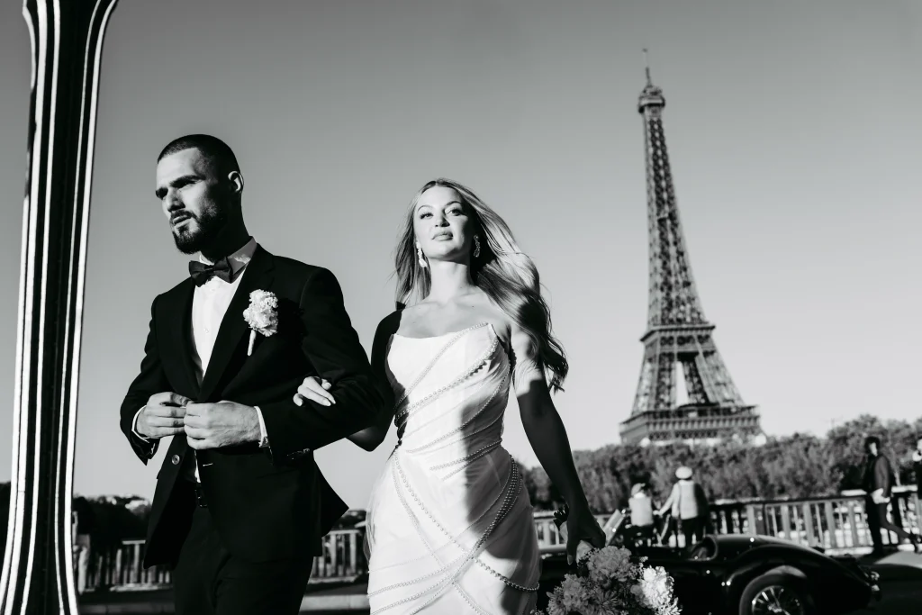 Brautpaar posiert neben einem weißen Oldtimer in Paris während Hochzeitsfotos.