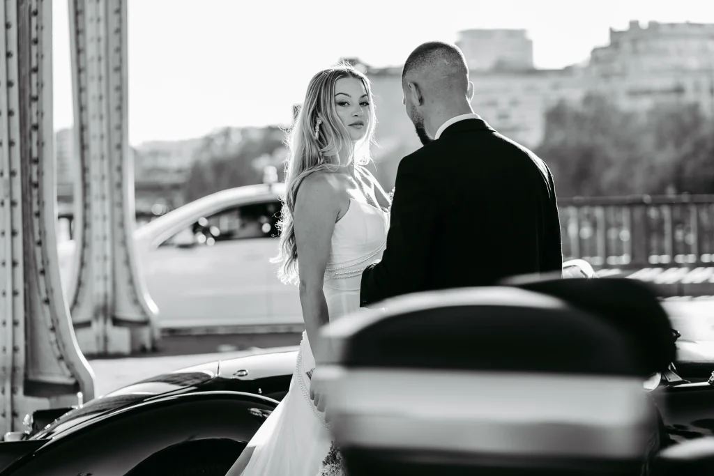 Braut hält Hand des Bräutigams neben Oldtimer in Paris während Hochzeitsfotos.